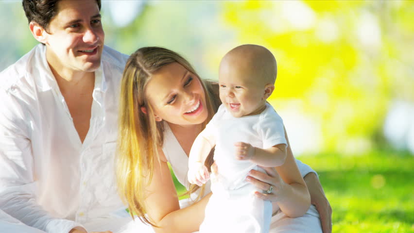 Close up smiling Caucasian parents sitting on grass in park holding up their cute young baby son shot on RED EPIC