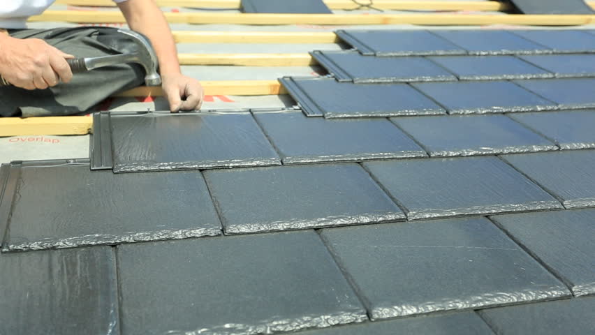 Roof tiler installing slate tiles on property roof