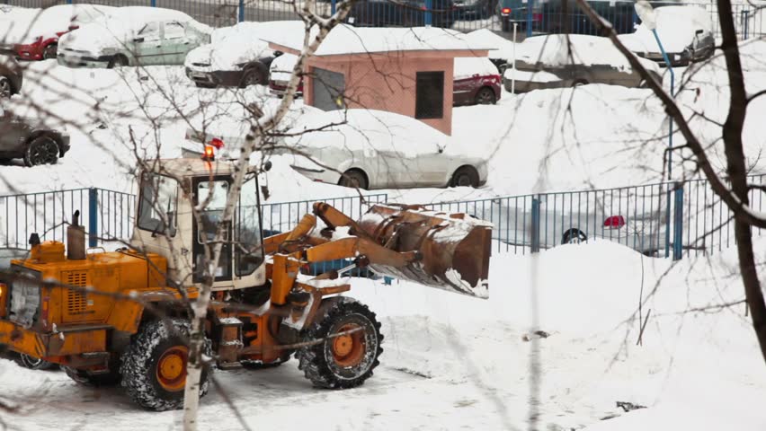 Bulldozer rides backward on small parking with few cars near road at winter day