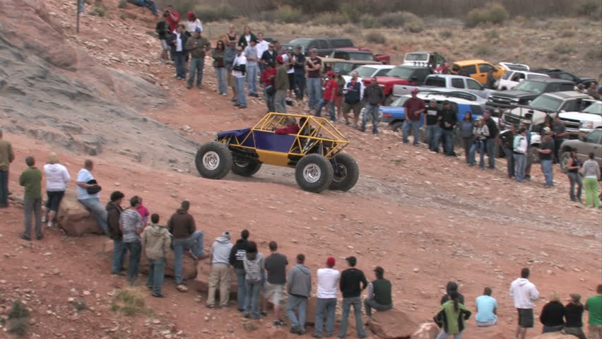Moab Utah Jeep Safari. Potato Salad rock hill with spectators watching modified purple and yellow buggy climbing steep rock ledge.