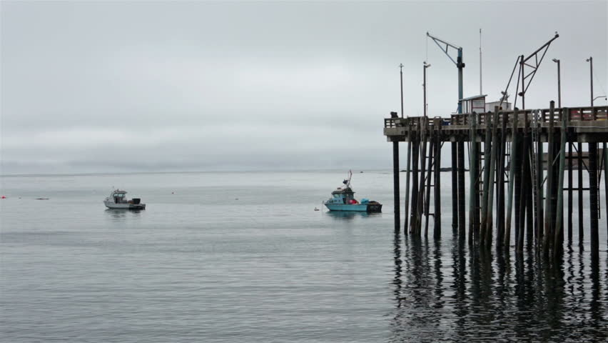 Ocean pier with man fishing two boats in cove rain mist. Annual Abalone fishing season first day open. Divers returning to shore after snorkeling and swimming to harvest seafood and shellfish