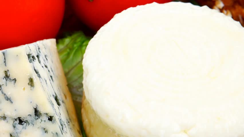 soft feta cheese with aged delicatessen cheeses on cutting wooden plate with tomatoes bread and olive oil