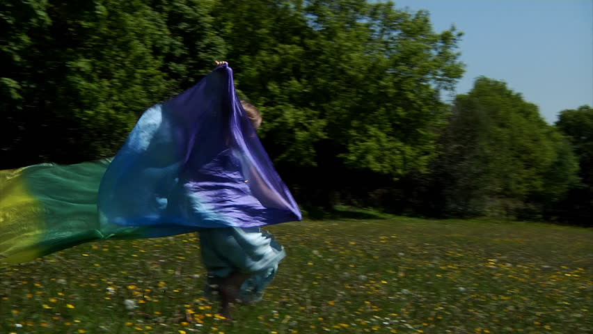 Little girl running down hill with a beautiful rainbow silk trailing behind her