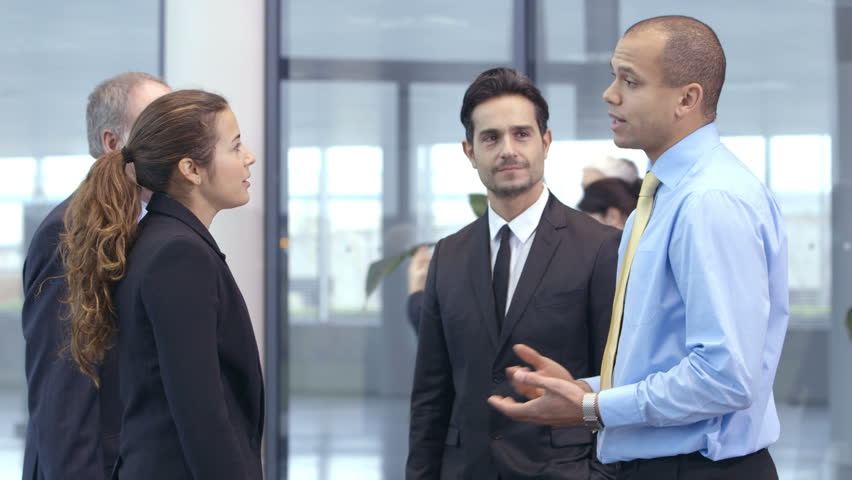 Confident and attractive business team of mixed ages and ethnicity meet and shake hands in the lobby of a busy modern office building. 