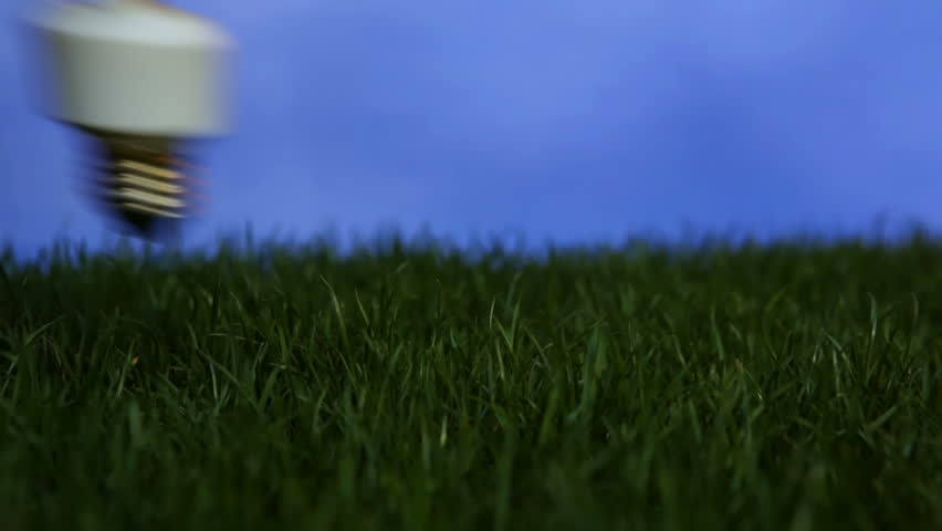 Compact fluorescent light bulb inserted into patch of grass and lighting up