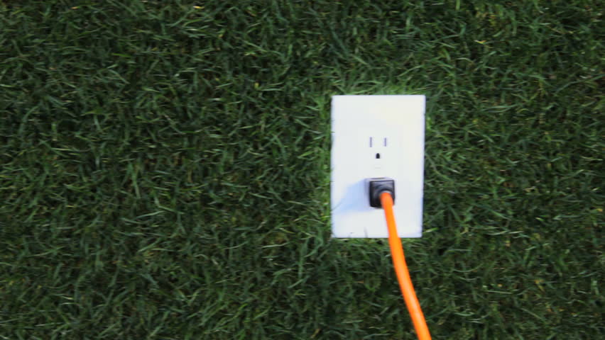 Cord plugged into electrical outlet in grass, dolly