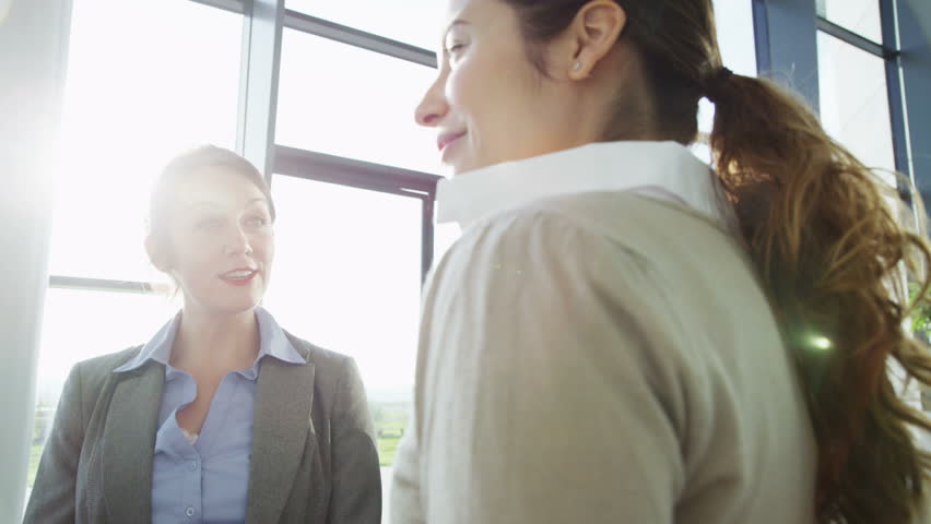 An attractive young business team are having a conversation in a bright, modern office building. They are bathed in sunlight which is streaming through the windows. In slow motion.
