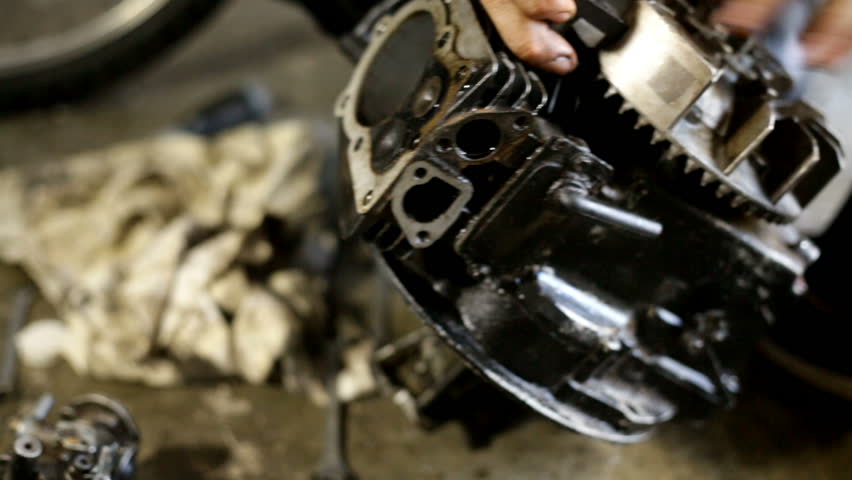 Young man cleaning a dirty engine of a mini motor. A lot of oil. Working in workshop on the floor. Unscrewing parts of the motor.