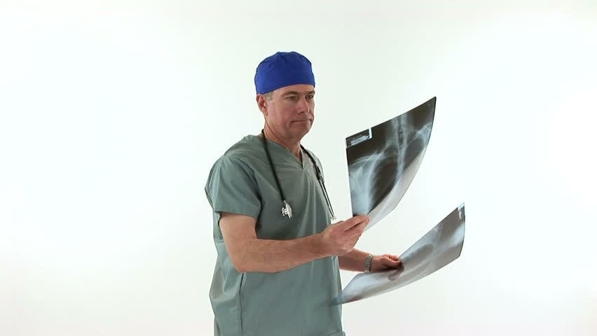 A doctor dressed in scrubs stops looking at the xrays and smiles at the camera.