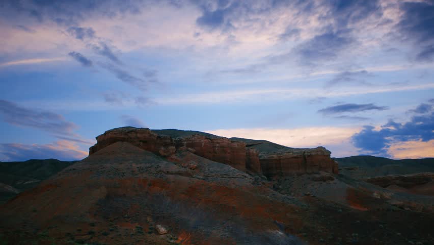 Timelapse over the Charyn (Timerlik) Canyon. Fluffy clouds above red rock mountain peak. Natural landscape erosion and grand canyons with stunning rock formations. silhouetted. 