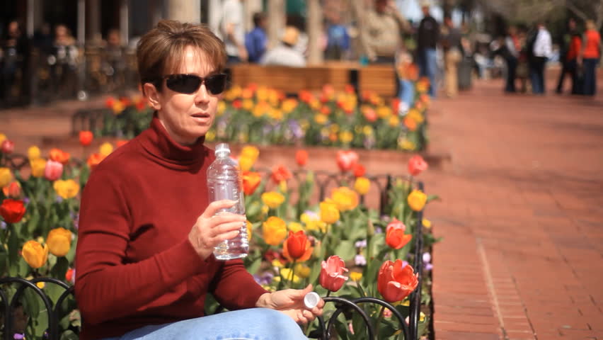 Multicolored tulips are the backdrop for a woman sitting and drinking water in a busy outside shopping mall.