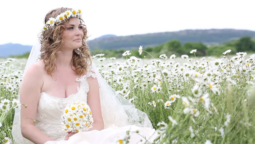 The beautiful bride lies in the field with chamomiles with a wreath on a head