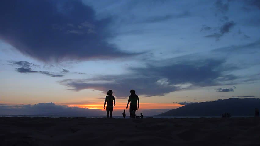 Unrecognizable people enjoying the evening sunset at the beach in Hawaii.
