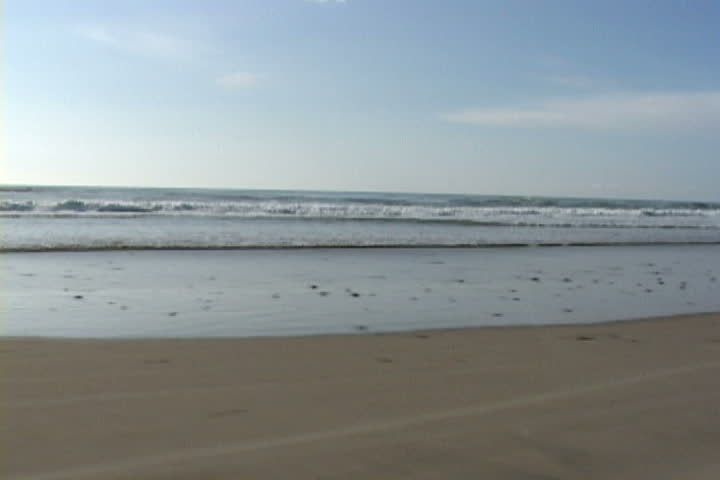 Vehicle drives on sandy, ocean shores in Oregon and parks to reveal mountainous rock around Cape Kiwanda.