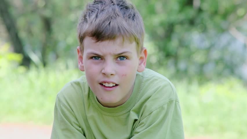 Young boy looks at background of foliage at summer day