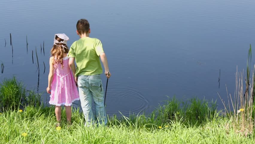 Two kids boy and little girl stand near pond and play with fishing rods