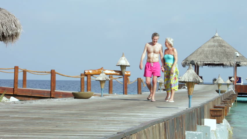 Senior Couple Walking On Wooden Jetty
