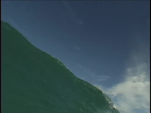 Water perspective of wave as it tubes and barrels towards the cliffs and beach. Perfect hawaiian wave rolling to shore.