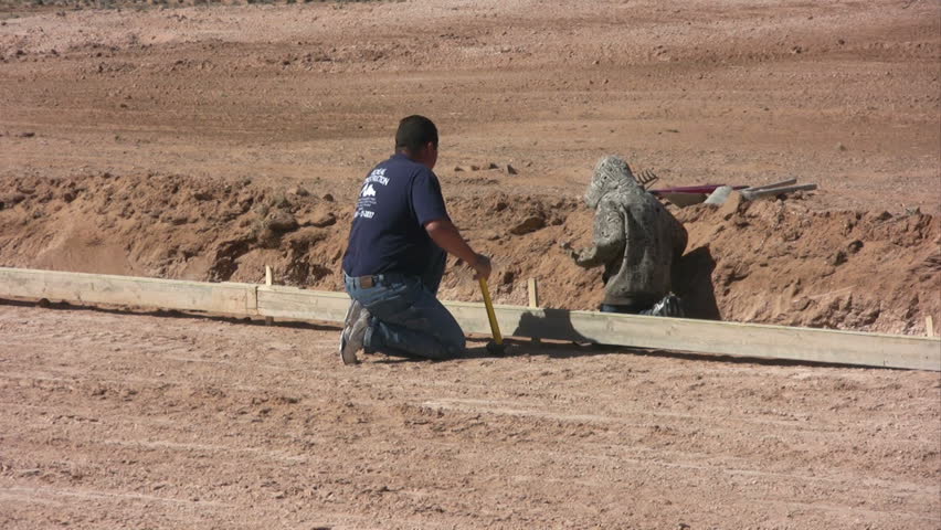 A man and his son work together to drive steel stakes for forms on a new home foundation.