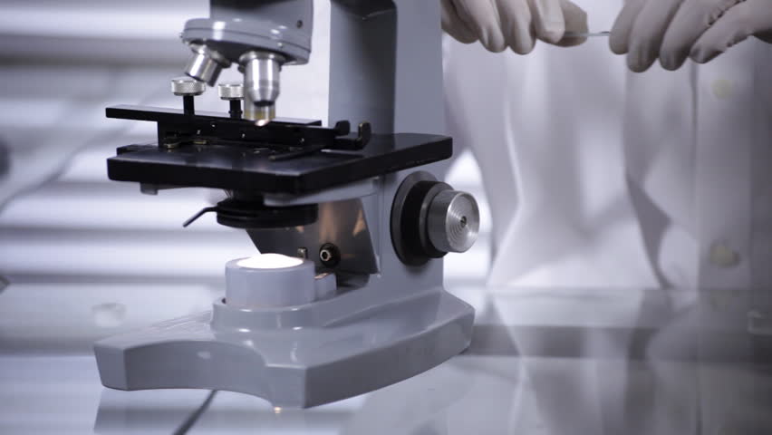 A young scientist, technician, or doctor examines a specimen he has placed under his microscope.