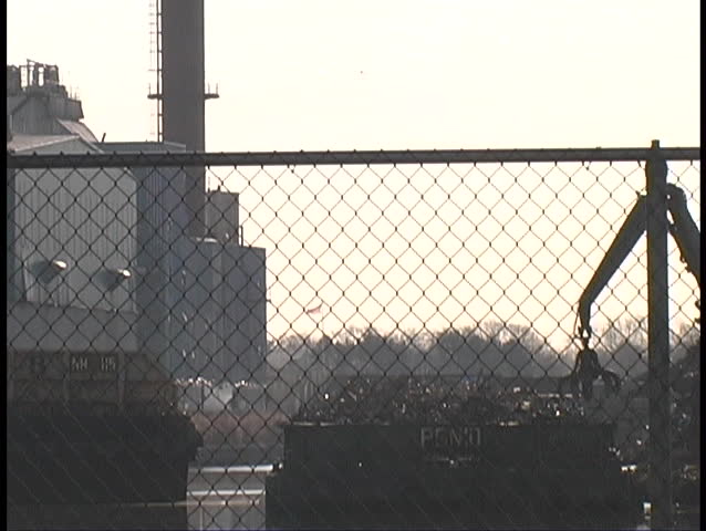 Crane picking garbage out of landfill over water in front of dump factory