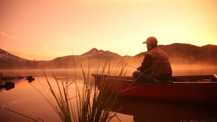 Man fishing in lake at sunrise