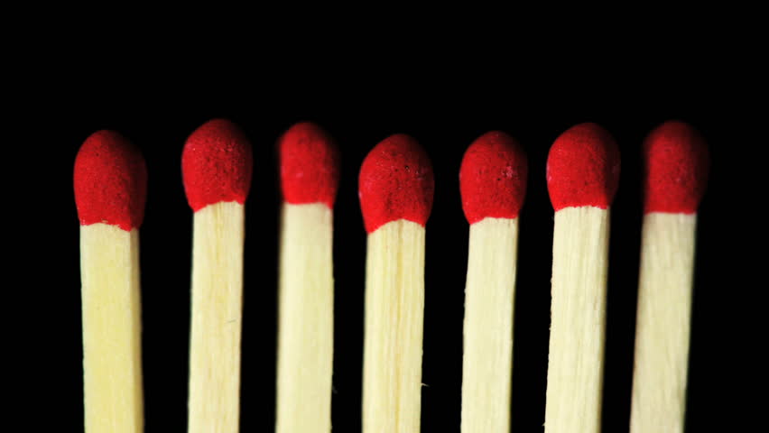 A close up of seven match at the point of ignition on a black background.