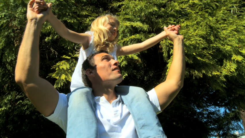 Young father tenderly holding his daughter on his shoulders while outdoors on a summers day