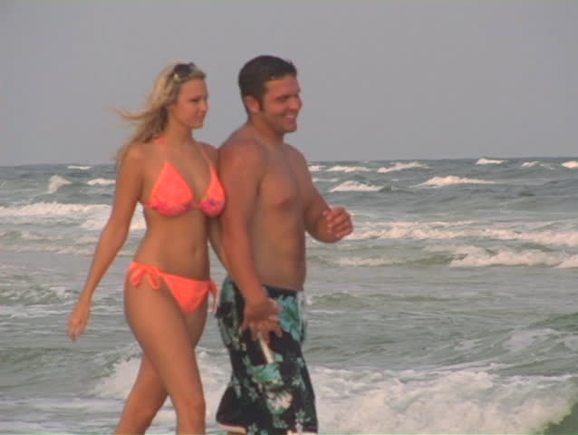 Couple medium shot holding hands and smiling. Walking in the edge of the water.