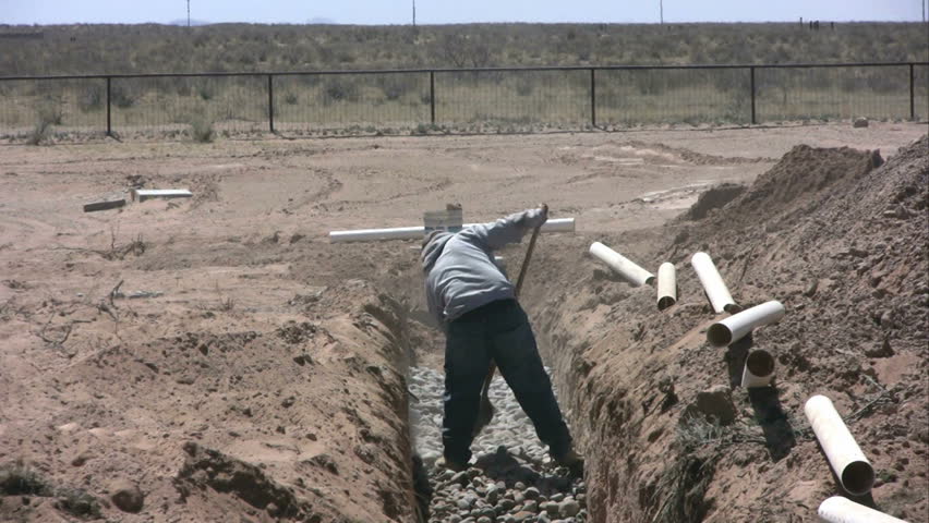 A man works with a shovel to level stones in a new drainfield.