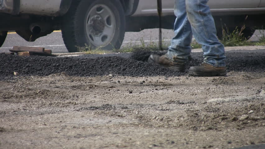 Man rakes and spreads hot asphalt.