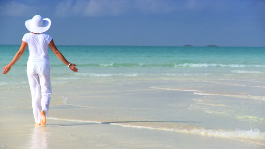Elegant young female walking on a beautiful white sandy beach looking at aquamarine waters 60 FPS