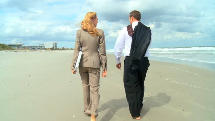 Two young business people escaping the office to walk on the beach 60 FPS