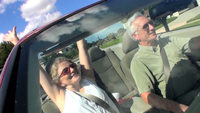 Contented retired couple enjoying driving home in the sunshine in their open top car