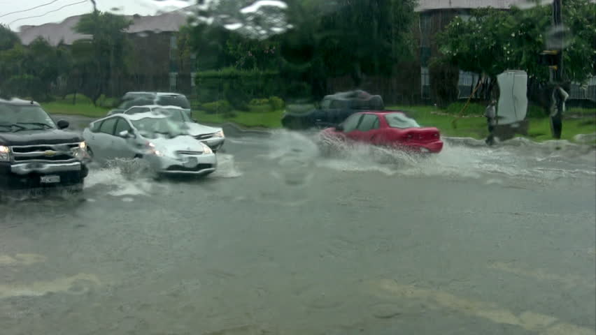 Video of flooded road intersection. Cars and trucks passing. Residential area. 
