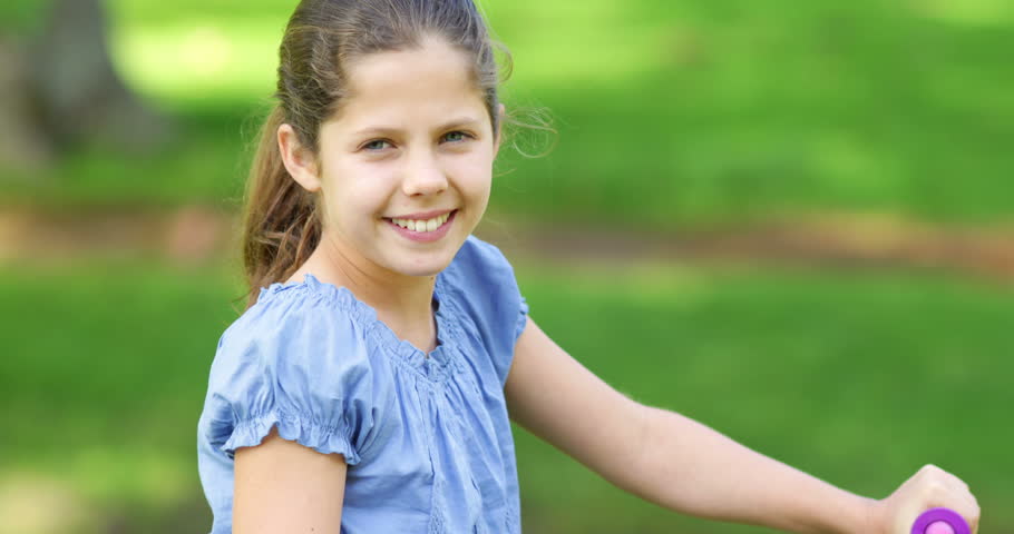 Little girl smiling and waving at camera on a pink bike on a sunny day