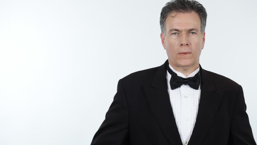 A man in formalwear, straightening his bowtie, checking his cufflinks, smoothing his lapels, and smiling with satisfaction.