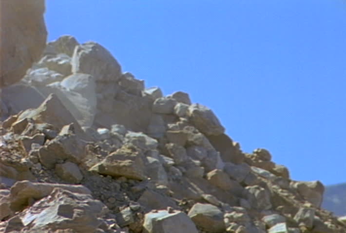 Boulders and smaller rocks roll and slide down a hill during a landslide.
