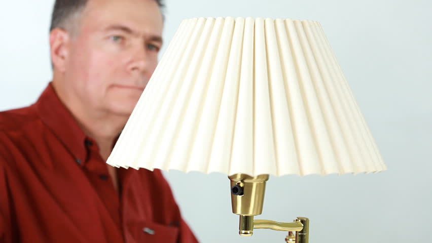 A man removes an incandescent bulb from a lamp and replaces it with a florescent energy efficient light bulb.
