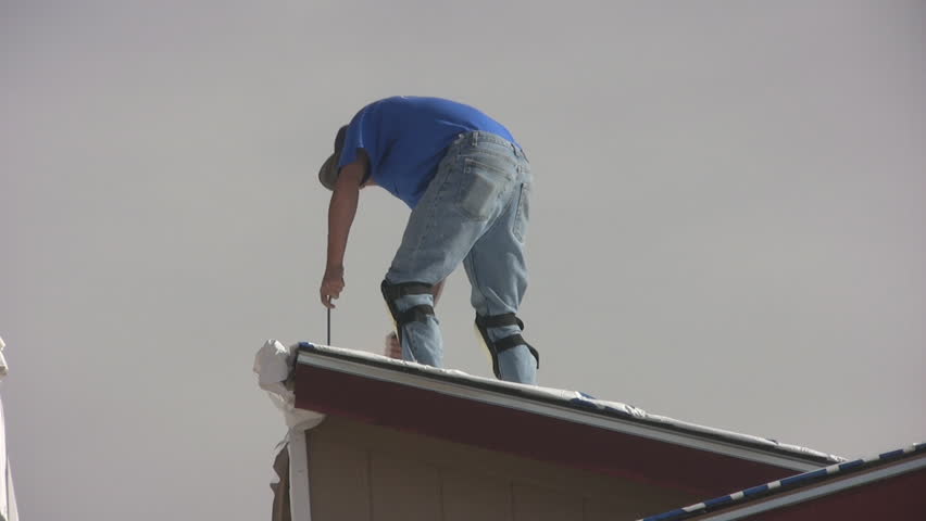 Hispanic man working on roof of new mobile home to remove shipping materials.