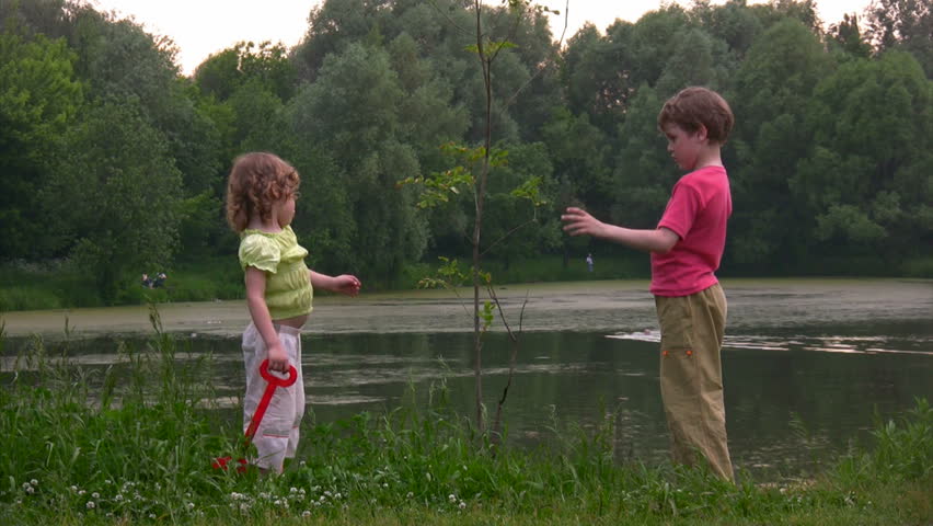boy with bucket and girl with shovel near young plant against pond 
