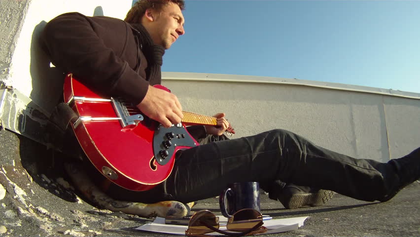 Musician with a guitar on the roof. The musician sits on the roof with his guitar and sings a song.