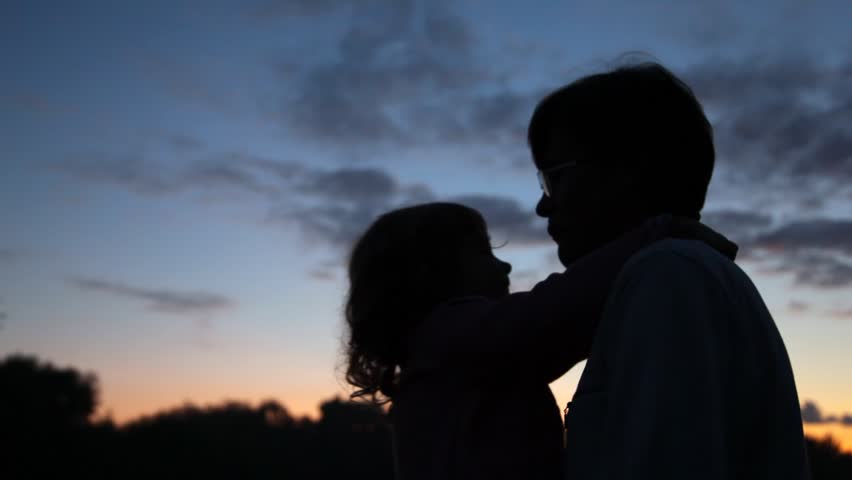 girl sits at daddy on hands on plays with it and rejoices in park at dawn of day 