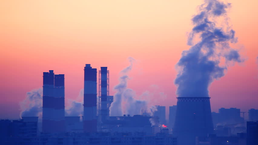 Smoke from smokestacks over cityscape at sunrise. HD 1080 seamless loop.