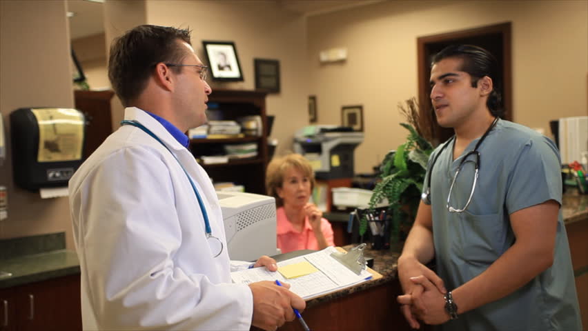 Two young doctors talking casually stop and smile for the camera.