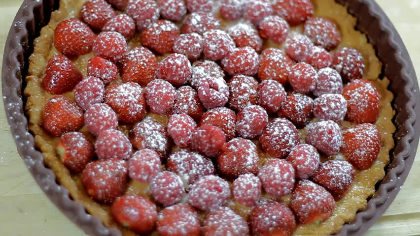 Sprinkling sugar onto rotating fruit tart
