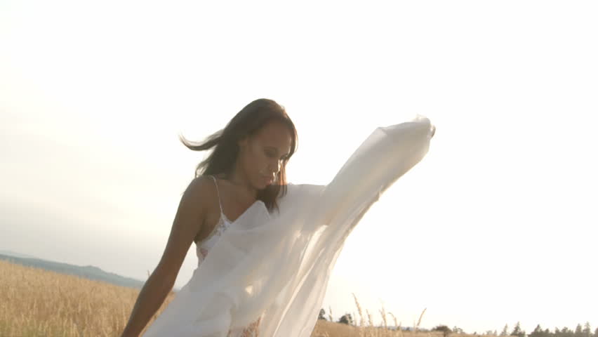A woman waves a sheer white sheet while moving around a wheat field.