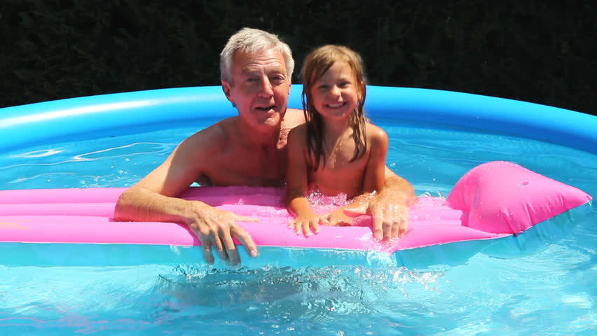 Grandfather and granddaughter splashing water on a lilo in a swimming pool