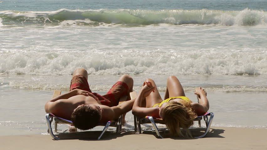 Young couple on lounge chairs holding hands by the ocean