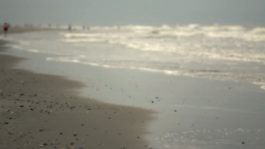 Waves wash up on shore on Isle of Palms (near Charleston, SC). Early morning on hazy day, people roaming in distant background. natural sound.